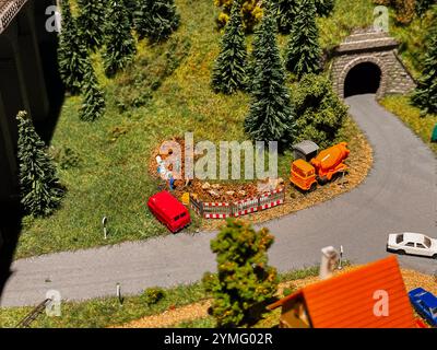 Eine Modelleisenbahn-Szene mit einem roten Auto, das in einen Haufen orangener Kegel gestürzt ist. Die Szene spielt in einem Wald mit einem kleinen Haus und einem Tunnel im B Stockfoto