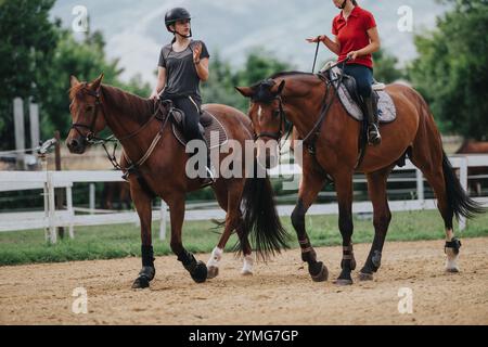 Zwei Mädchen, die auf einer Ranch Pferde reiten, Helme tragen und über Reittraining im Freien diskutieren Stockfoto