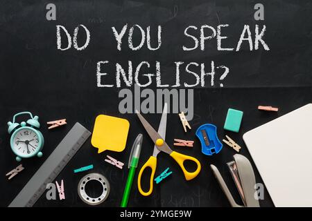 Tafel mit den Worten Do you speak English darauf. Die Tafel ist mit verschiedenen Schulmaterialien wie Schere, einem Lineal und einem bedeckt Stockfoto