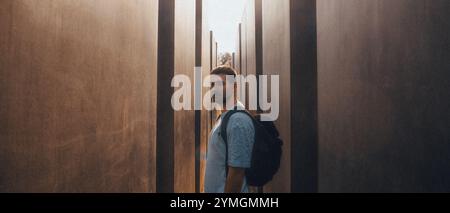 Ein Mann mit einem großen Rucksack steht in einem langen, schmalen Flur zwischen zwei hohen Bäumen, die Schatten und Atmosphäre spenden Stockfoto