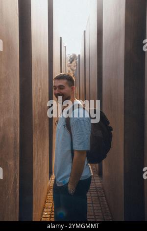 Ein Mann mit einem großen Rucksack steht in einem langen, schmalen Flur zwischen zwei hohen Bäumen, die Schatten und Atmosphäre spenden Stockfoto