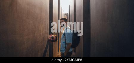 Ein Mann mit einem großen Rucksack steht in einem langen, schmalen Flur zwischen zwei hohen Bäumen, die Schatten und Atmosphäre spenden Stockfoto