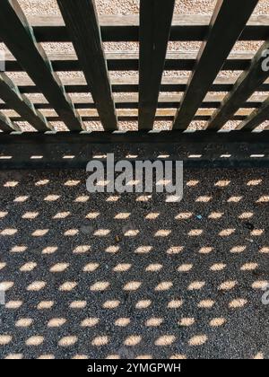 Ein Schatten eines hölzernen Zauns auf einem Betonboden. Der Schatten besteht aus vielen kleinen Punkten, die ein interessantes und einzigartiges Muster erzeugen Stockfoto