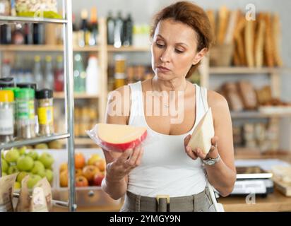 Die Frau wählt sorgfältig leckeren Käse in der Lebensmittelabteilung des Supermarktes aus Stockfoto