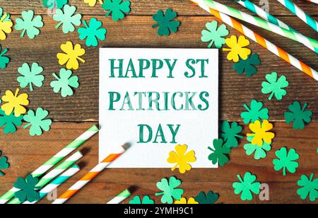 Das Schild zum Happy St. Patrick's Day steht auf einem Tisch mit grünem und gelbem Kleeblatt. Das Schild ist umgeben von Strohhalmen und Klee Stockfoto