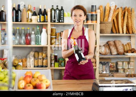 Die Verkäuferin für Erwachsene bietet Wein im Lebensmittelgeschäft an Stockfoto