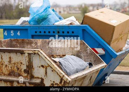 Rostige Müllcontainer gefüllt mit Bauschutt und Müllsäcken auf einer Außenfläche. Abfallentsorgung und Baustellenmanagement Stockfoto