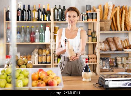 Die Verkäuferin für Erwachsene bietet Wein im Lebensmittelgeschäft an Stockfoto