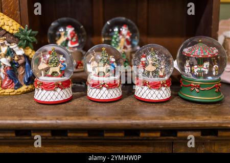 Glaskugeln mit Weihnachtsfiguren, in Wasser mit Schnee gelegt, auf einer Holzschrankplatte. Stockfoto