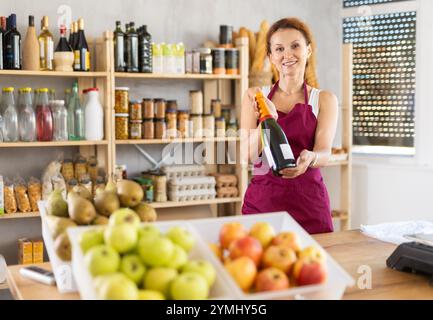 Die Verkäuferin für Erwachsene bietet Wein im Lebensmittelgeschäft an Stockfoto