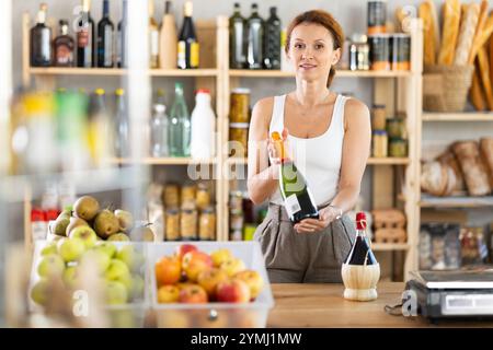 Die Verkäuferin für Erwachsene bietet Wein im Lebensmittelgeschäft an Stockfoto