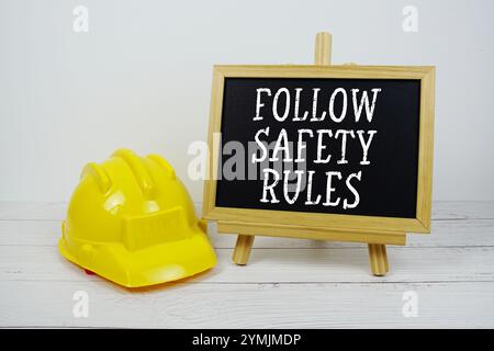Befolgen Sie den Text der Sicherheitsregeln auf der Tafel mit einem Schutzhelm auf hölzernem Hintergrund Stockfoto