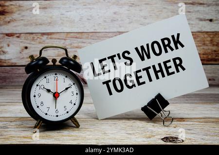 Arbeiten wir zusammen Text auf Papierkarte mit Wecker auf hölzernem Hintergrund Stockfoto