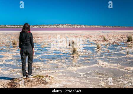 Eine einzige weibliche Touristenwandererin steht auf einem kleinen Hügel am Rande einer salzverkrusteten Kante um einen Pink Lake in Western Australia. Stockfoto