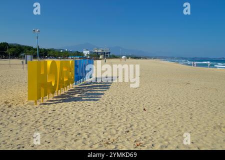 Yangyang County, Südkorea - 3. November 2024: Ein einzigartiger Blick auf das Schild Hajodae Beach, das lange Schatten auf den Sandstrand wirft, mit weit entfernten mountai Stockfoto