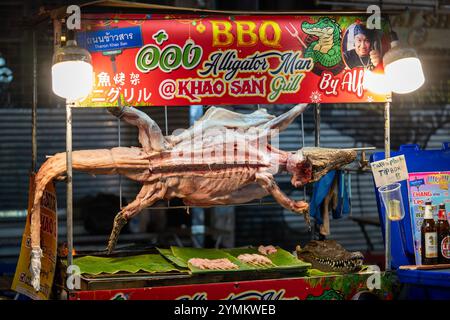 Ein Straßenverkäufer stellt auf einem geschäftigen Nachtmarkt in der Khao San Road in Bangkok, Thailand, einen ganzen Alligator zum Grillen vor. Stockfoto