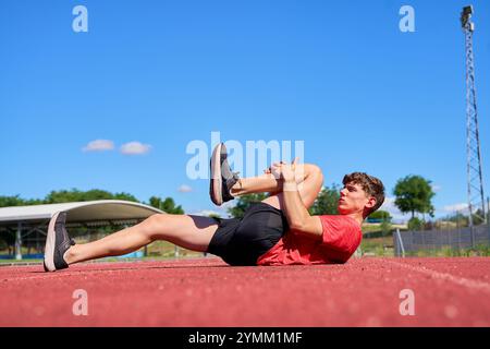 Ein Mann liegt auf dem Boden mit gebeugtem Bein und Fuß auf dem Knie. Er trägt ein rotes Hemd und schwarze Shorts Stockfoto