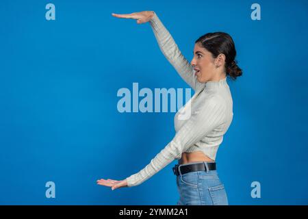 Junge Frau, die mit Händen die Größe von etwas auf blauem Hintergrund zeigt Stockfoto