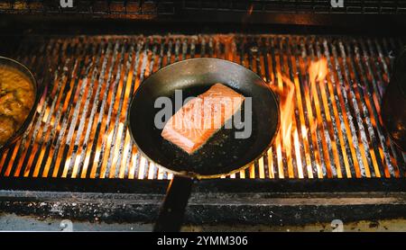 Eine Pfanne Lachs kocht auf einem Grill. Der Lachs befindet sich mitten auf dem Grill und ist von Flammen umgeben Stockfoto