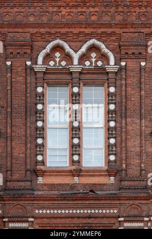 Ein Fragment der Mauer eines alten Backsteingebäudes mit einem Fenster, das mit einem gemusterten Rahmen eingerahmt ist. Stockfoto