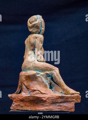 Kleine Terrakotta-Statuette, die eine stilisierte weibliche Figur auf einem Felsen darstellt, von hinten gesehen, vor dunklem Hintergrund Stockfoto