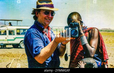 Kaukasischer Tourist zeigt einem maasai in traditionellem rotem Gewand einen Camcorder in tansania, afrika Stockfoto