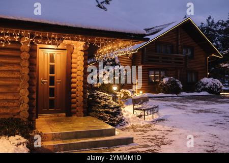 Bezaubernder Holzeingang, beleuchtet von festlichen Lichtern, schneebedeckten Treppen und friedlicher Winterumgebung. Stockfoto