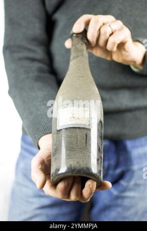 Nahaufnahme von der Hand eines Mannes, der eine alte Weinflasche staubig hält Stockfoto