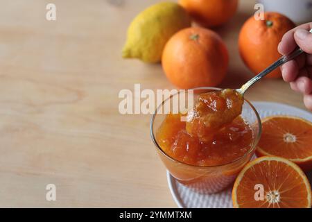 Hand mit Löffel, hausgemachte frische Orangenmarmelade in eine Glasschale, Kopierraum Stockfoto