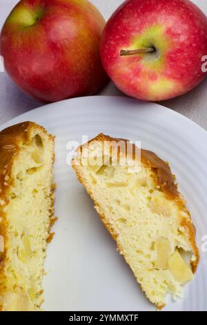 Köstliche Apfelkuchenscheibe auf weißem Teller und zwei roten Äpfeln Stockfoto
