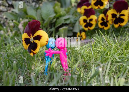 Lustige Souvenirfiguren treffen sich gerne im Gras neben großen Stiefmütterchen Stockfoto