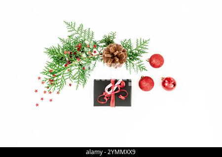Frohe Weihnachtskomposition mit Tannenzweigen, schwarzer Geschenkbox und roten Kugeln mit Konfetti auf weißem Hintergrund. Flache Lage, Draufsicht Stockfoto