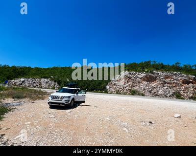 Zadar, Kroatien - 14. November 2024: Ein weißer Geländewagen parkt auf einer felsigen Straße vor einem Hintergrund von üppigem Grün und klarem blauem Himmel, der an Themen erinnert Stockfoto