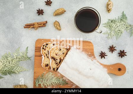 Festliches Stillleben mit traditionellem Weihnachtsstollenkuchen auf einem Holzbrett, einer Tasse schwarzen Kaffee, Zimtstangen, Anissternen, goldenen Tannenzapfen, A Stockfoto