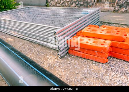 Stapel, Haufen von verzinkten Teilen für temporäre Metallzaunplatten werden gestapelt und ein hohler Kunststoffzaunfuß auf der Straße, bereit für die Montage am Bau Stockfoto