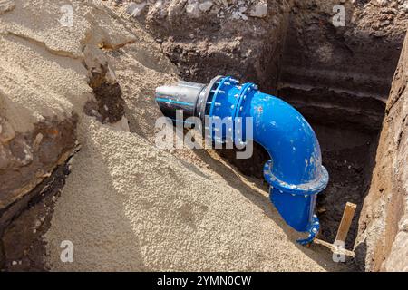 Kupplung mit Schrauben zur Verbindung von großen Rohrleitungen, Kunststoffrohr mit Metallbogen der unterirdischen Wasserversorgung. Unvollendetes Projekt, unverschütteter Graben Stockfoto