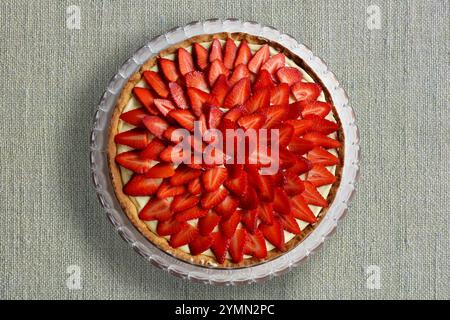 Frischer Obstkuchen dekoriert mit Erdbeerscheiben, Blick von oben, Leinenstruktur Hintergrund Stockfoto