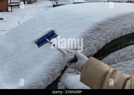 Eine Frau schaufelt Schnee aus dem Auto, entfernt Eis von der Karosserie, Winterangriff, bereitet das Auto auf die Route vor Stockfoto