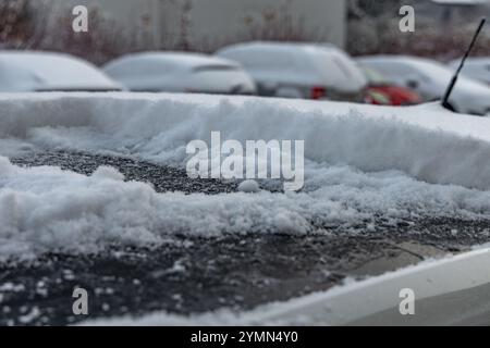 Eine Frau schaufelt Schnee aus dem Auto, entfernt Eis von der Karosserie, Winterangriff, bereitet das Auto auf die Route vor Stockfoto