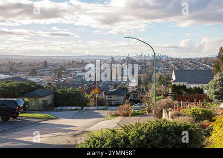 Eine ruhige Vorstadtstraße in Burnaby Heights mit Häusern und geparkten Autos bietet einen Fernblick auf Vancouvers weitläufige Skyline Stockfoto