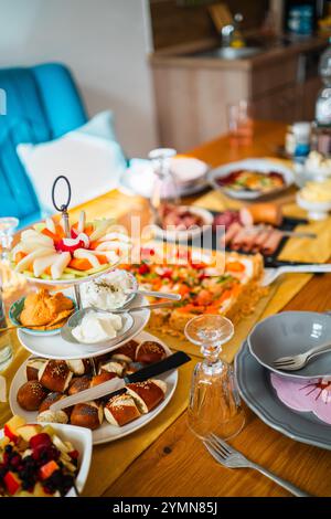 Ein lebhafter Brunch mit frischem Gebäck, einer farbenfrohen Obstplatte, cremigen Dips und köstlicher Pizza, wunderschön auf einem Holztisch arrangiert Stockfoto