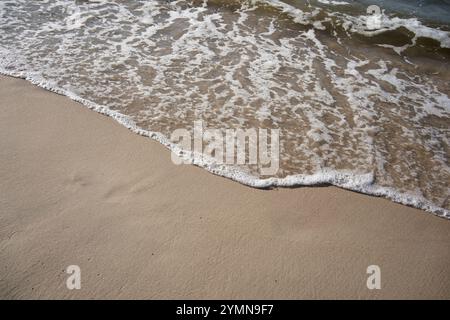 Sanfte Meereswellen, die über den Sandstrand strömen, Nahaufnahme mit natürlichem Licht. Stockfoto