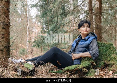 Eine Frau ruht in einem Kiefernwald, lehnt sich an einen Baumstumpf. Nach oben schauen. Stockfoto