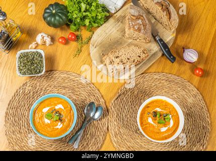 Teller mit Kürbissuppe und Croutons auf strukturierten ökologischen Ständen werden auf einem Holztisch platziert, auf dem Gemüse, ein Kürbis, ein Schneidebrett mit sl stehen Stockfoto