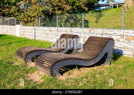 Zwei stationäre Sonnenliegen am Stadtstrand. Grüner Rasen und Gabion im Hintergrund. Stockfoto