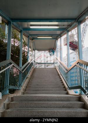 Treppe, die zu einem erhöhten Gehweg führt, mit Stadtbau im Hintergrund, die städtische Infrastruktur und Fortschritt miteinander verbindet Stockfoto