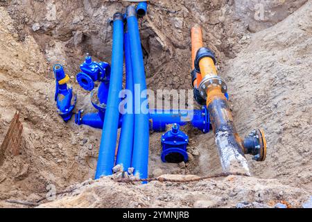 Verlegung neuer Wasser- und Kabelrohre für die Stadtkommunikation. Reparaturgrube. Blaue und orangefarbene Rohre. Stockfoto