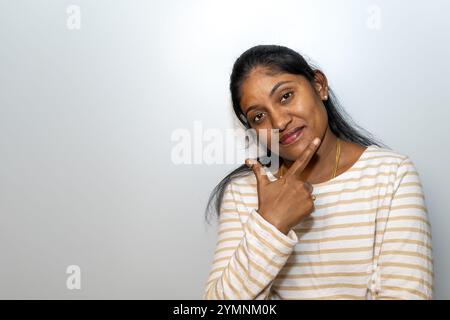 Eine südasiatische Frau strahlt Selbstvertrauen und Stil aus und posiert vor neutralem Hintergrund. Stockfoto