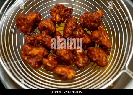 Würzige, knusprige Blumenkohlröschen, die in einem Metallkorb abfließen. Perfekt für vegetarische Vorspeisen, Snacks oder Beilagen. Stockfoto