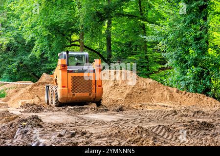 Ein orangefarbener Minilader entfernt Schmutz aus dem Park. Stockfoto